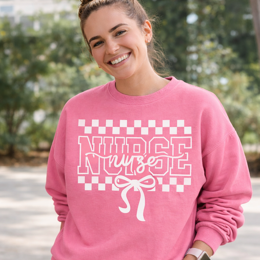 Woman wearing a pink sweatshirt with 'Nurse' text and checkered design outdoors.